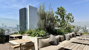 A rooftop terrace with outdoor seating, including a sofa and tables, surrounded by greenery and overlooking a cityscape. - Mi Zona Lodging Reforma (Mexico City)