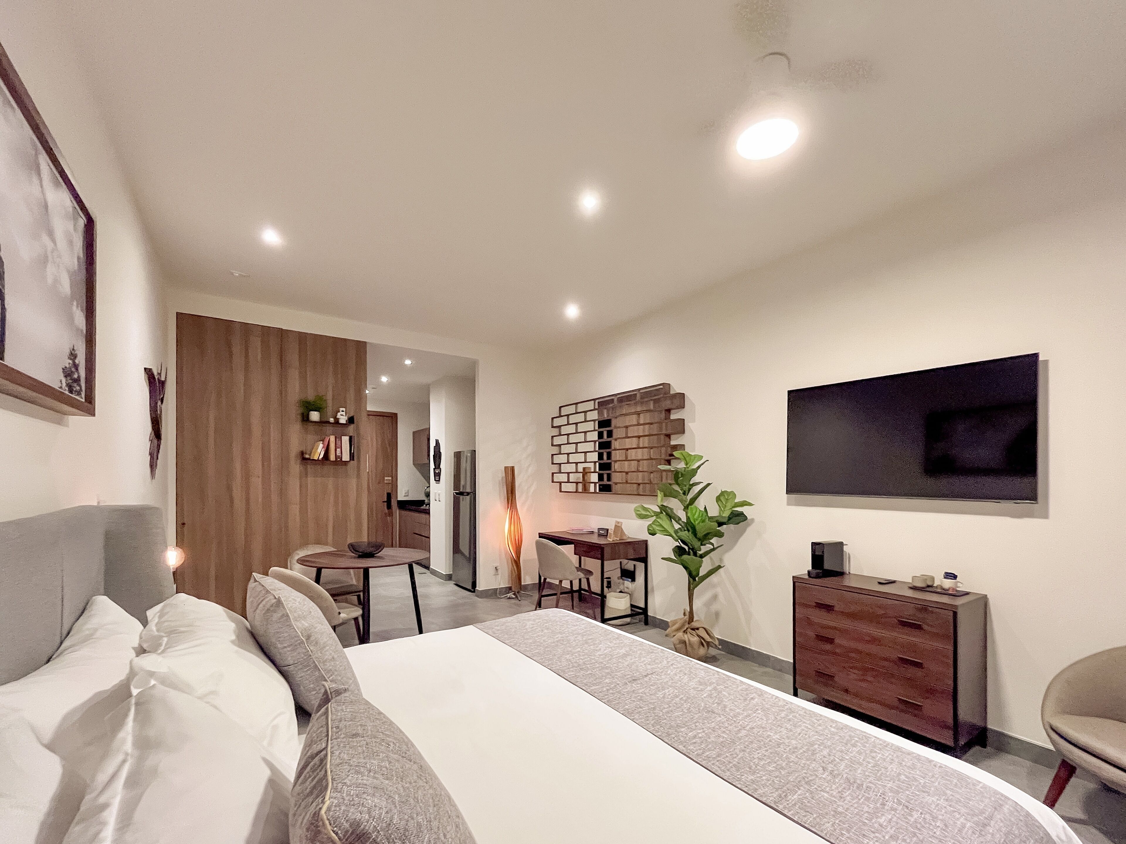 A modern bedroom with a large bed, a desk, and a TV.