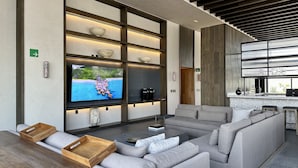 A modern living room with a large flat-screen TV, grey sofas, wooden side tables, and a kitchen area visible through a large window. - Mi Zona Lodging Reforma (Mexico City)