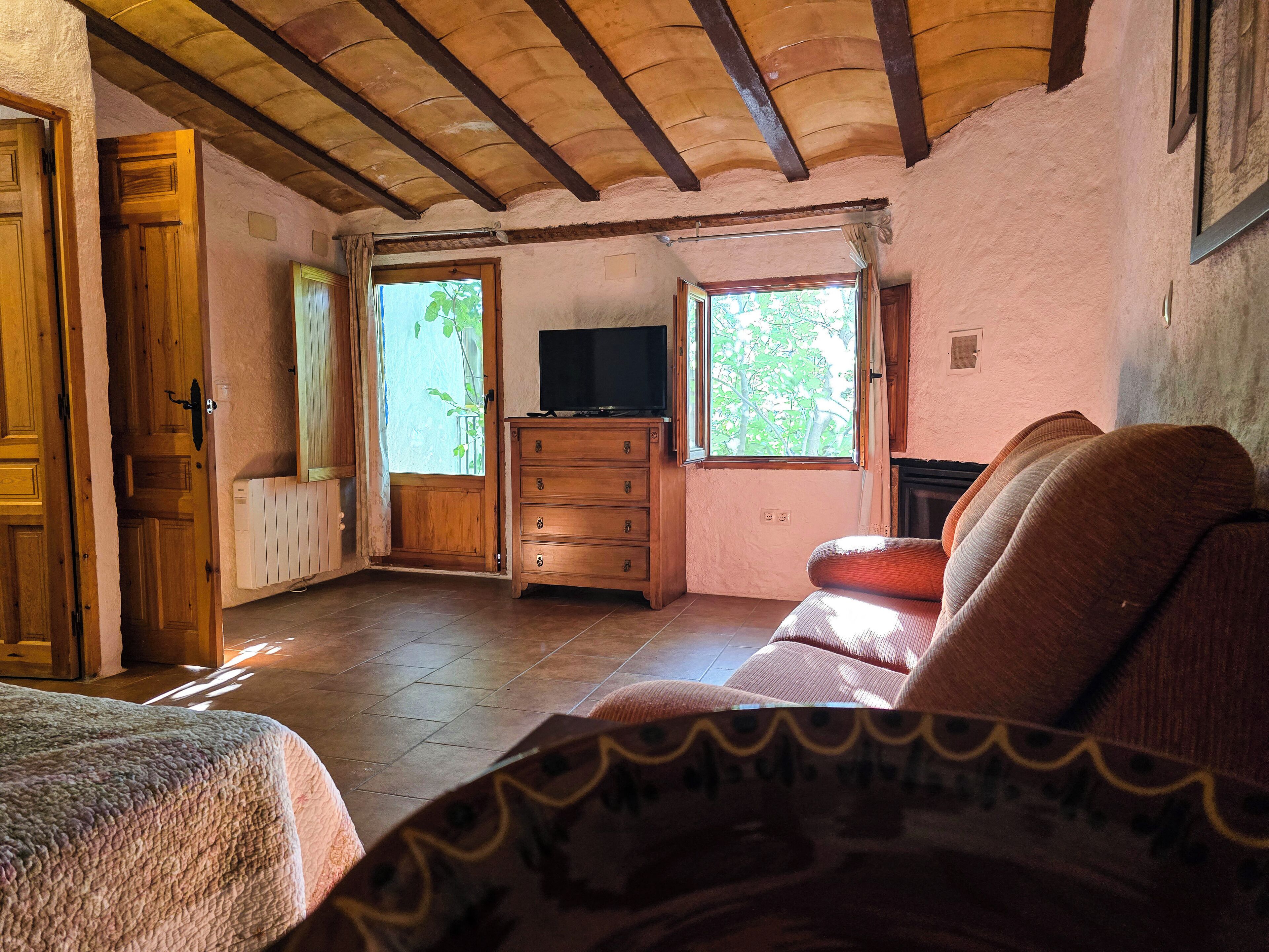 Una habitación acogedora con techo de madera, un televisor sobre un mueble de madera, un sofá y una ventana con vistas a árboles.
