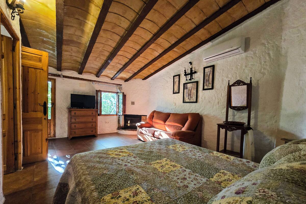 A cozy room with a fireplace, a sofa, a TV, and a bed with a floral quilt.
