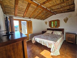 Un dormitorio con techo de madera, una cama con ropa de cama floral, una mesita de noche de madera y una ventana con contraventanas de madera.