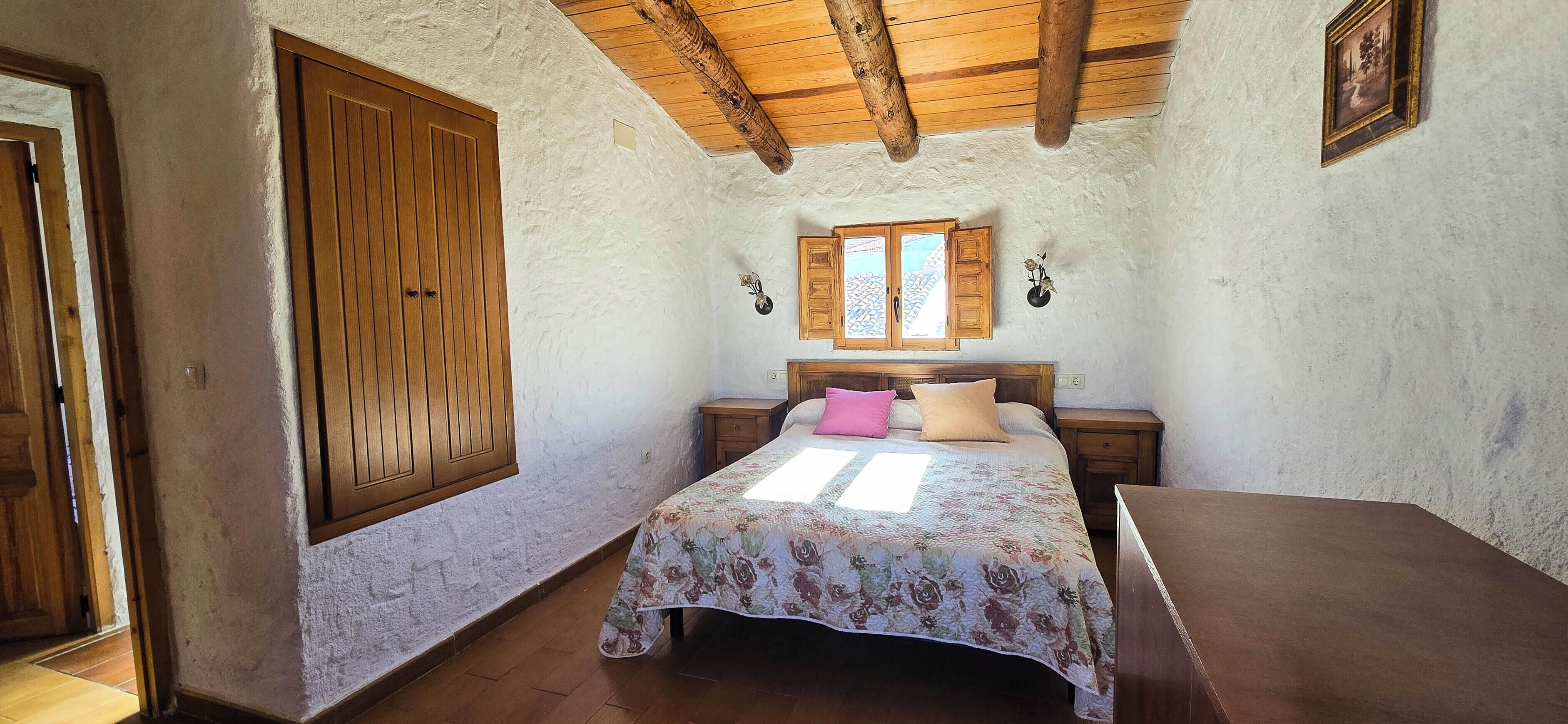 Quarto com cama de madeira, mesa de cabeceira, guarda-roupa de madeira e janela com persianas.