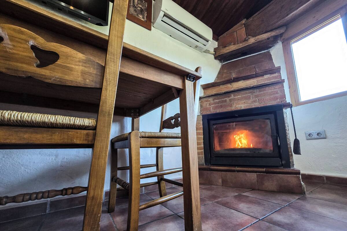 A rustic interior with a wooden table, a chair, a fireplace, and a window.