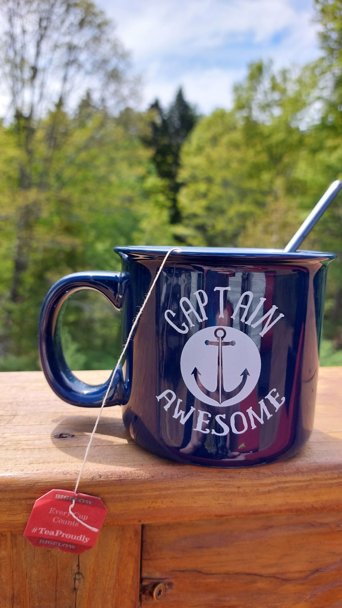 A metal mug with a handle, labeled 'CAPTAIN AWESOME,' and a tea bag hanging from it.