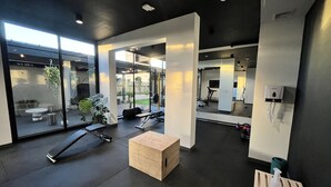 Een moderne sportschool met trainingsapparatuur, een houten bank en grote ramen met uitzicht op de omgeving.