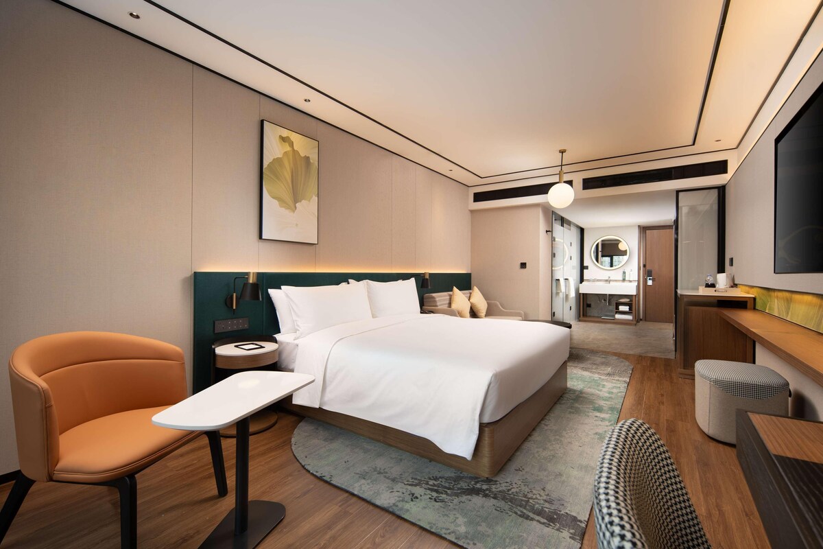 Habitació d'hotel moderna amb un llit gran, un escriptori, una cadira i una televisió.