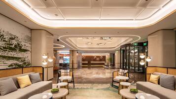 A modern lobby with seating areas, a reception desk, and a glass elevator.