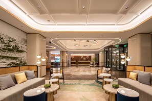 A modern lobby with seating areas, a reception desk, and a glass elevator. - Hilton Garden Inn Beijing West Railway Station (Beijing)
