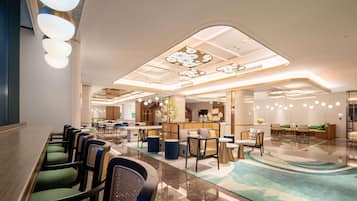 A modern hotel lobby with a long reception desk, seating area with chairs and sofas, and a decorative ceiling with recessed lighting.