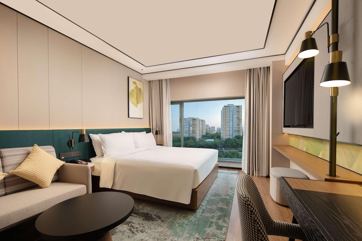 Una habitación de hotel moderna con una cama grande, un sofá, una mesita de café y un televisor montado en la pared.