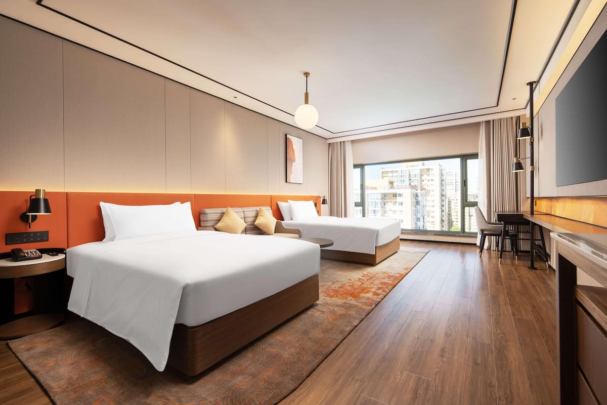 Habitación de hotel con dos camas, un escritorio, un televisor y un ventanal con vista a la ciudad.