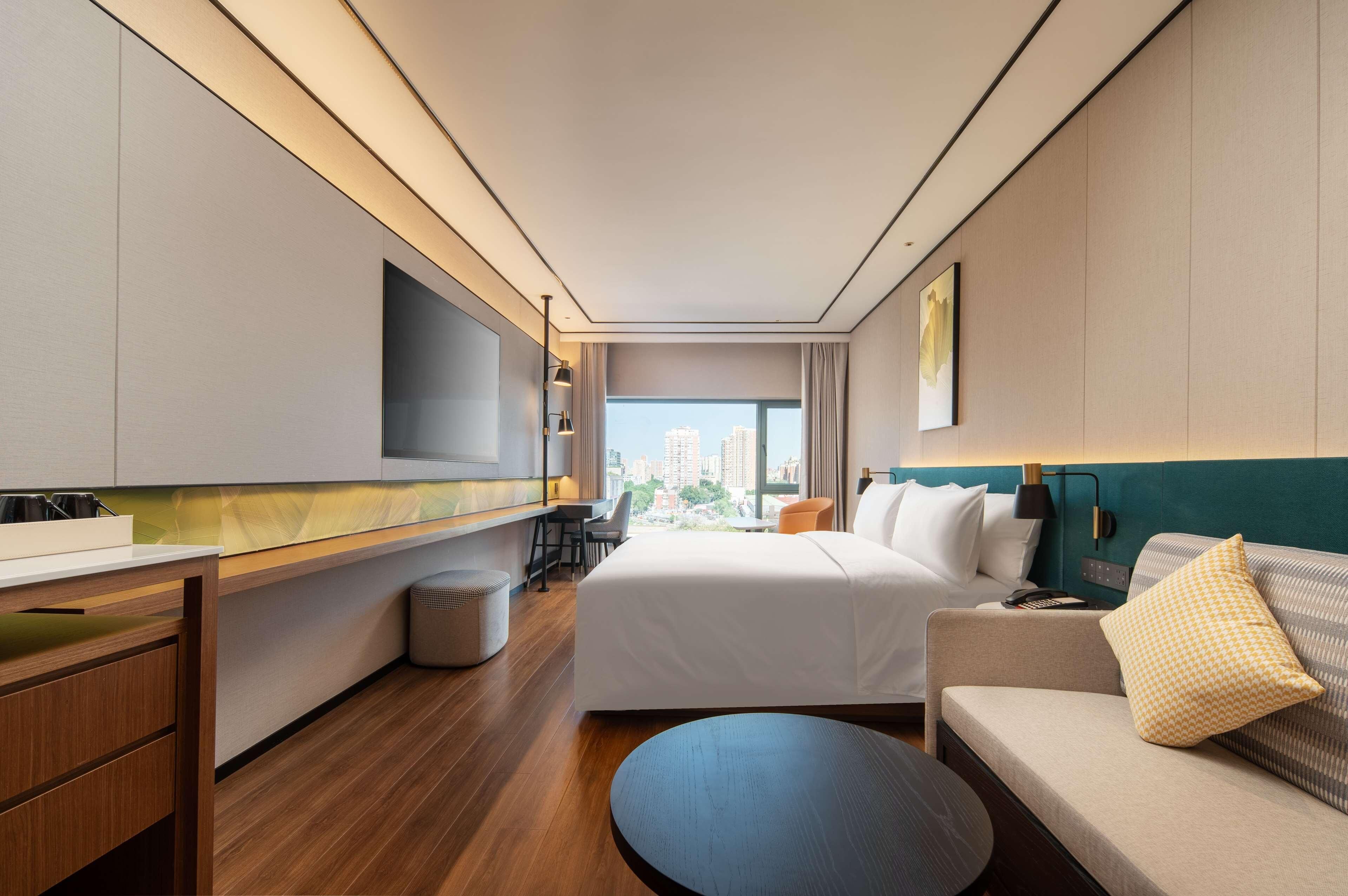 Una habitación de hotel moderna con una cama grande, un sofá, un escritorio y un televisor montado en la pared.