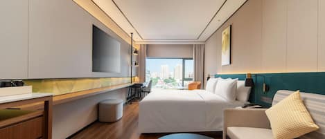 Una habitación de hotel moderna con una cama grande, un sofá, un escritorio y un televisor montado en la pared.