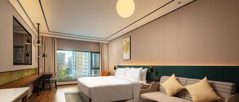 A modern hotel room with a large bed, a sofa, a desk, and a view of the city.