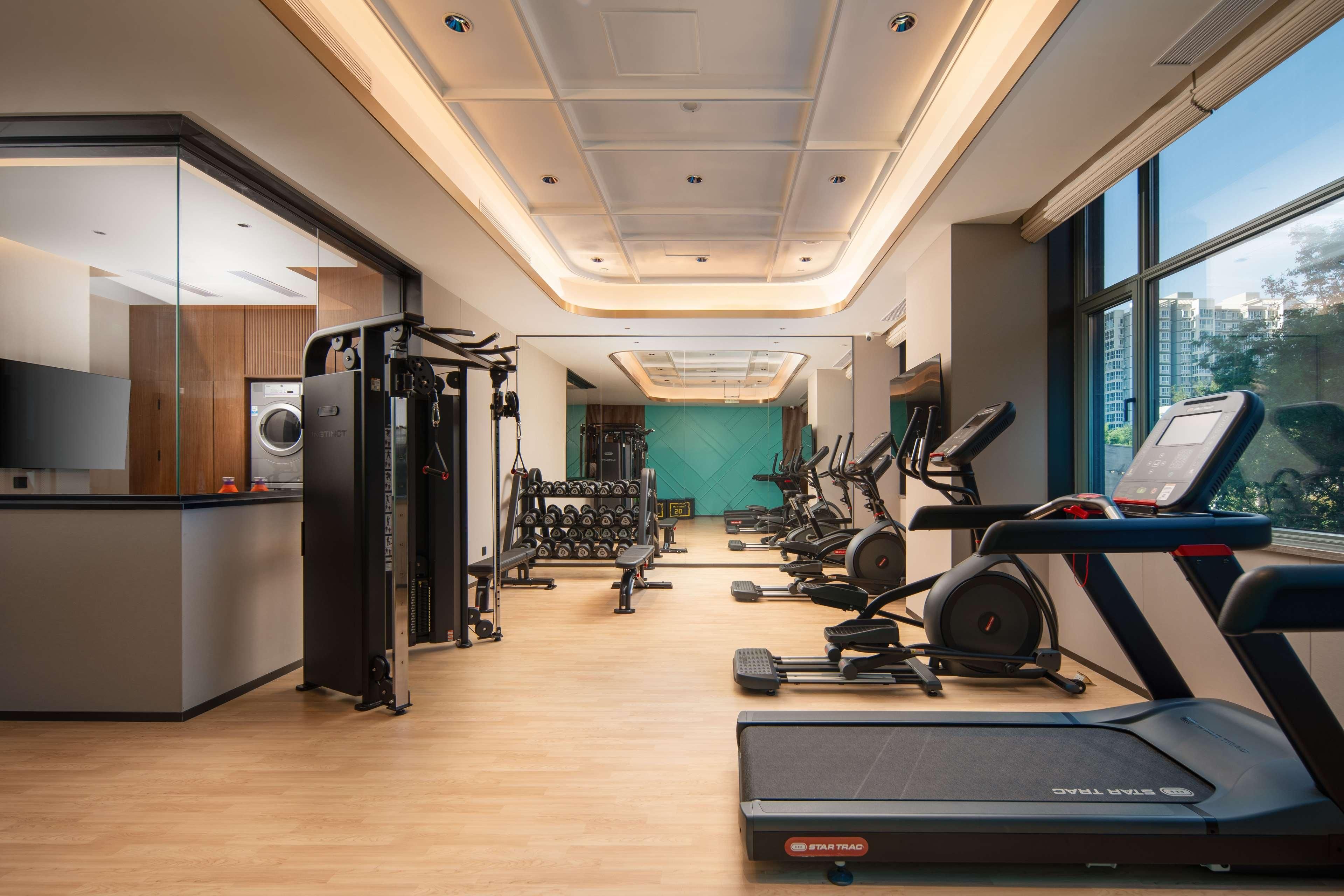 Uma academia moderna com equipamentos de cardio, máquinas de peso e uma parede verde.