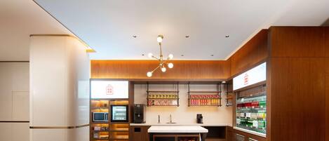 Un moderno vestíbulo de hotel con un mostrador central, máquinas expendedoras y una vitrina refrigerada.