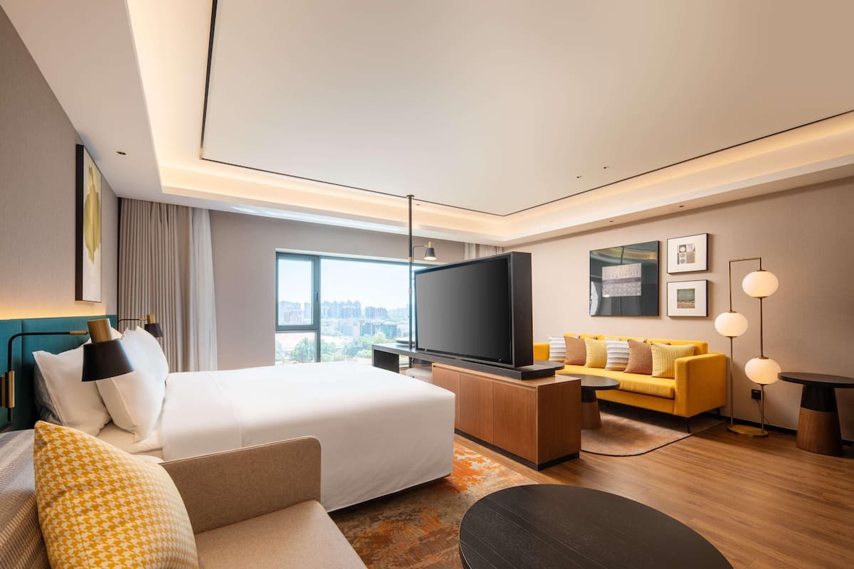 Habitación de hotel moderna con una cama grande, un sofá, un televisor y vistas a la ciudad.