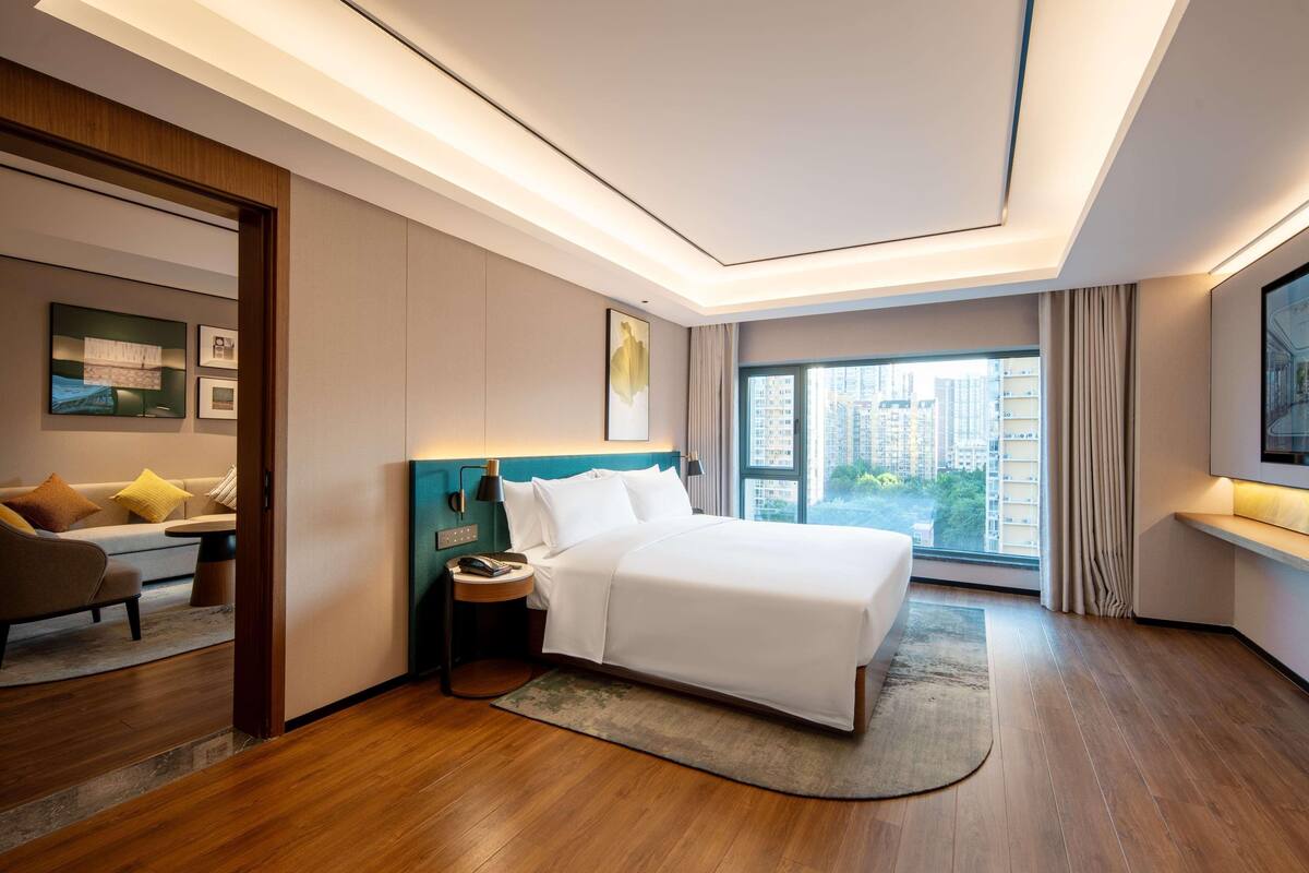 Una habitación de hotel moderna con una cama grande, un escritorio, un sofá y vistas a la ciudad a través de amplios ventanales.