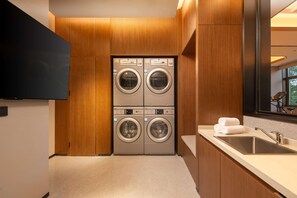A modern laundry room with two front-loading washing machines, a sink, and a mirror. - Hilton Garden Inn Beijing West Railway Station (Beijing)
