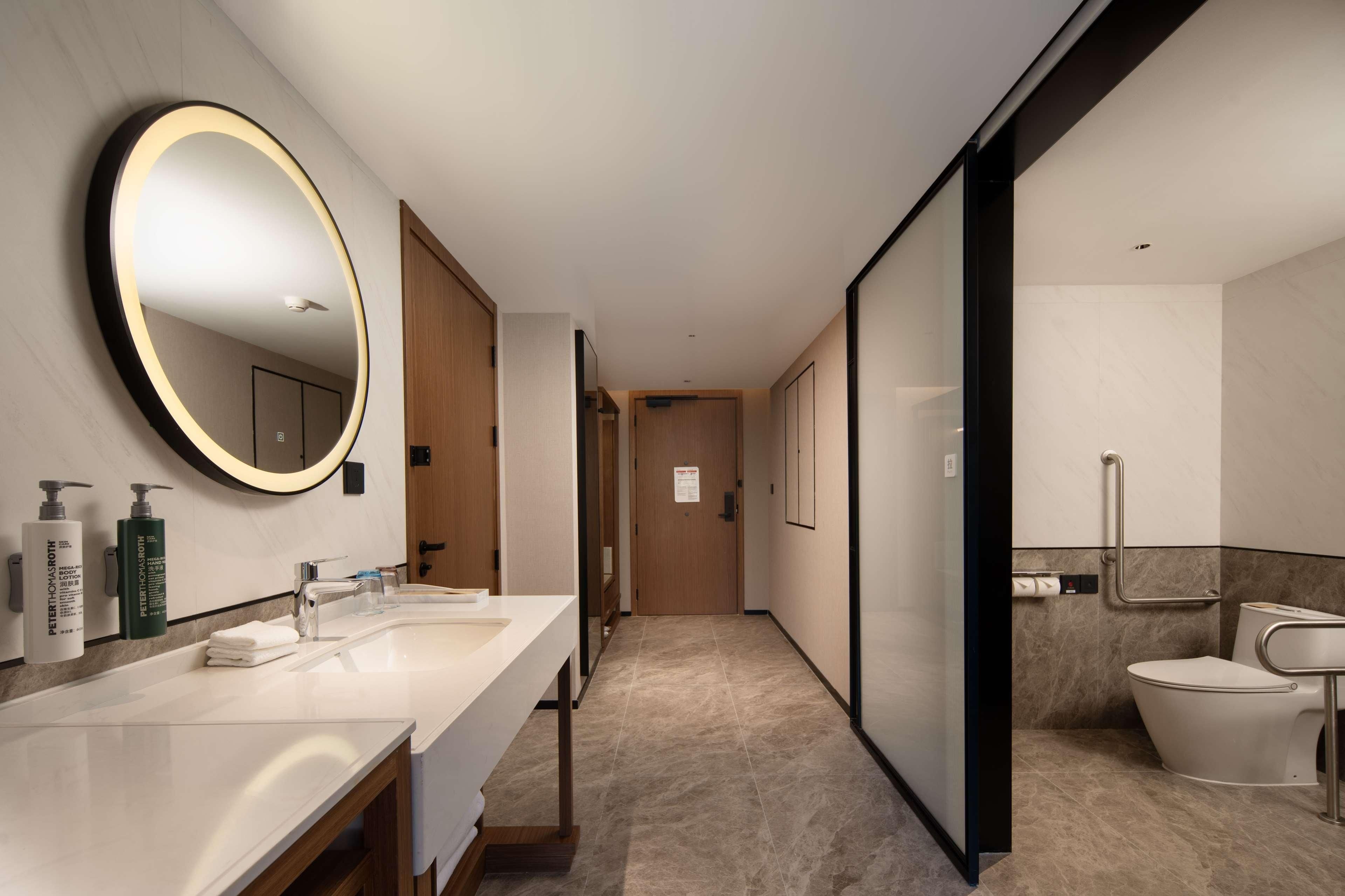 A modern hotel bathroom with a large mirror, two sinks, a toilet, and a shower area.
