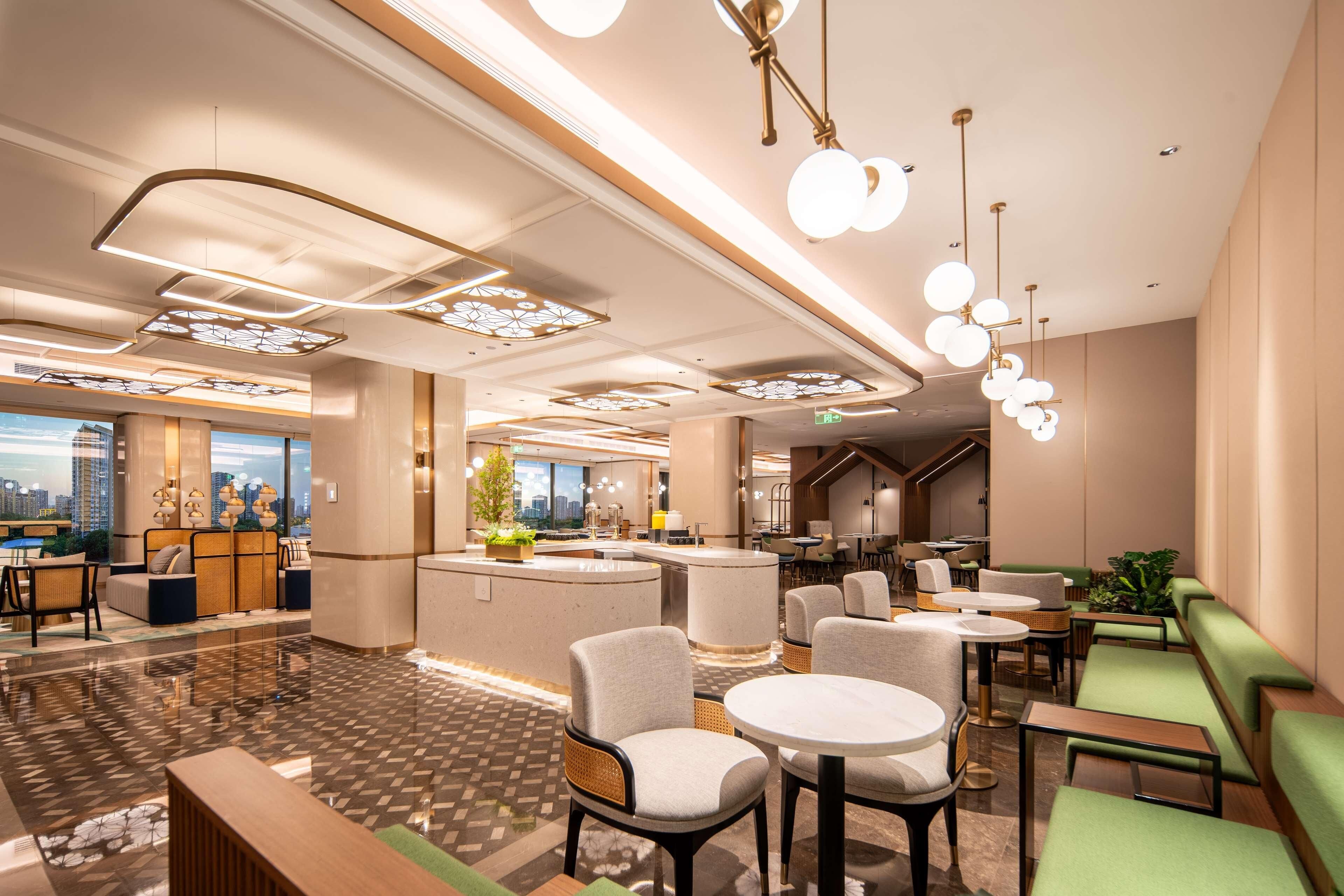 A modern hotel lobby with a central bar, seating areas, and a view of the cityscape.