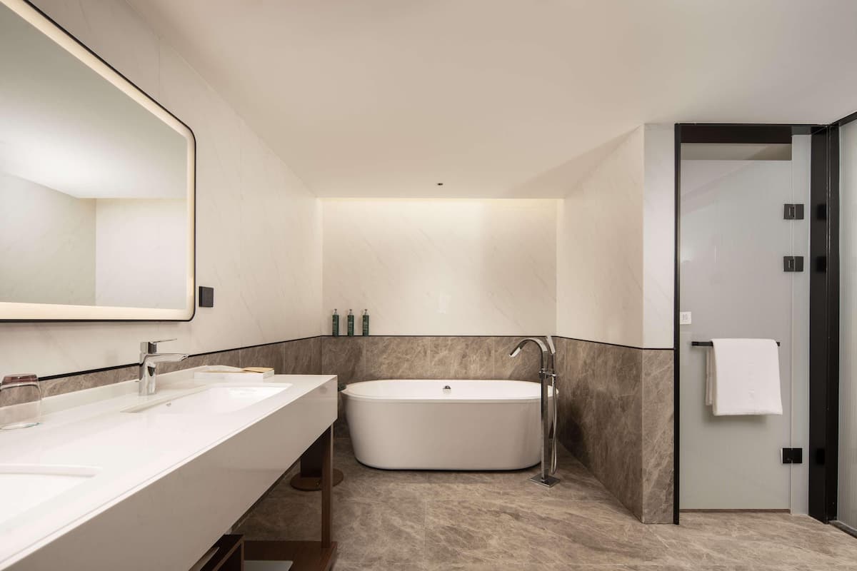 Un baño moderno con un espejo grande, dos lavamanos, una bañera y una ducha a pie.