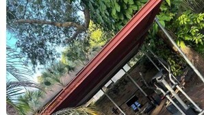 Un espacio al aire libre techado con equipo de ejercicio, un edificio de ladrillo y palmeras.