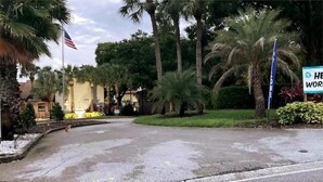 A curved driveway leading to a building with palm trees and a flag.
