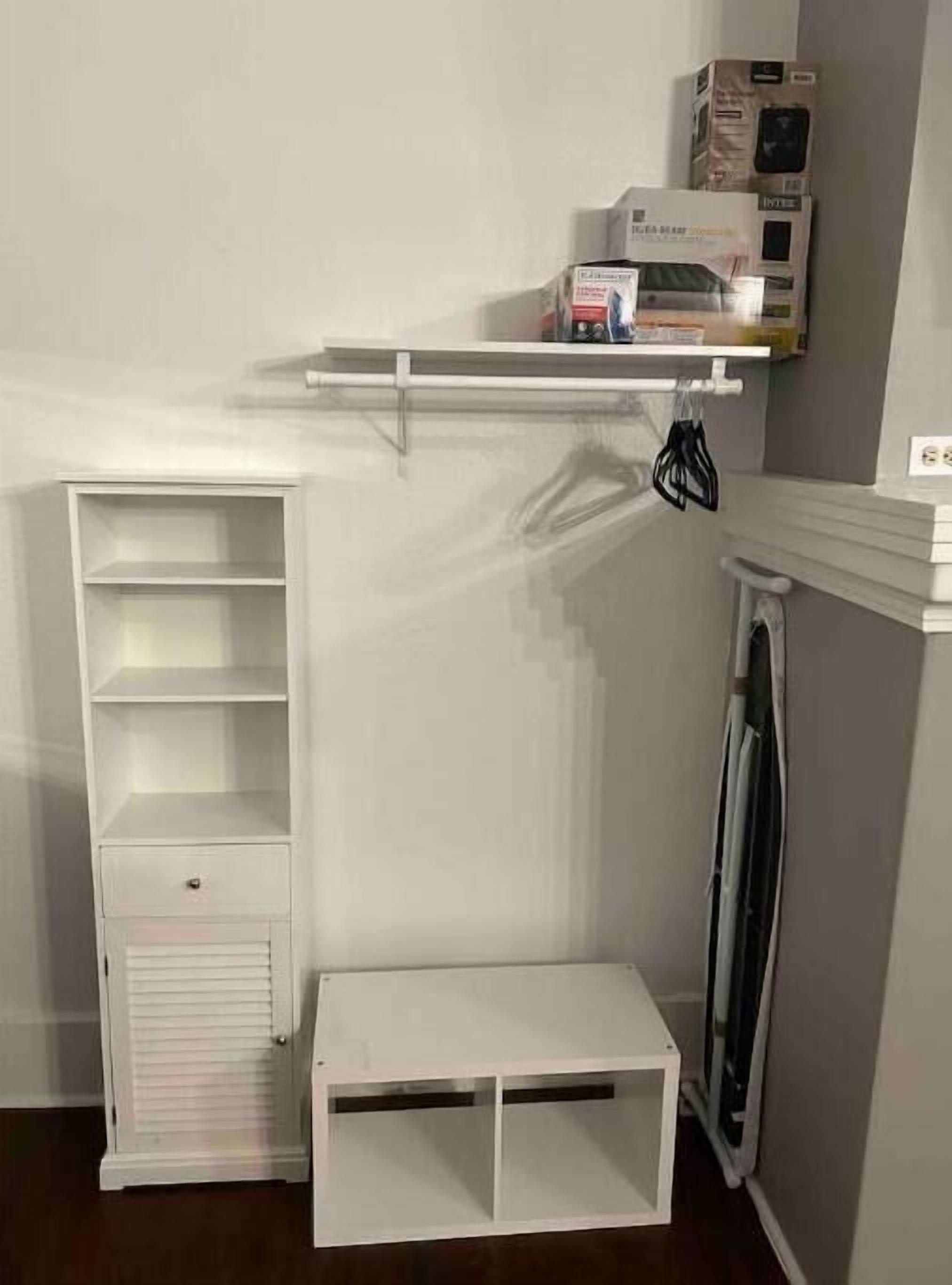 Un meuble de rangement blanc, doté d’étagères et d’un petit placard, un radiateur blanc et une étagère avec des boîtes et un objet noir.