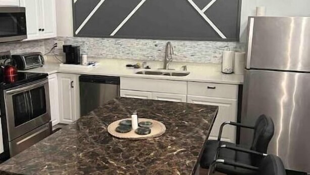 A modern kitchen with a central island, white cabinets, a stainless steel refrigerator, and a black and white geometric backsplash.
