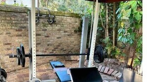 A covered outdoor gym with a bench press, dumbbells, and weight plates.