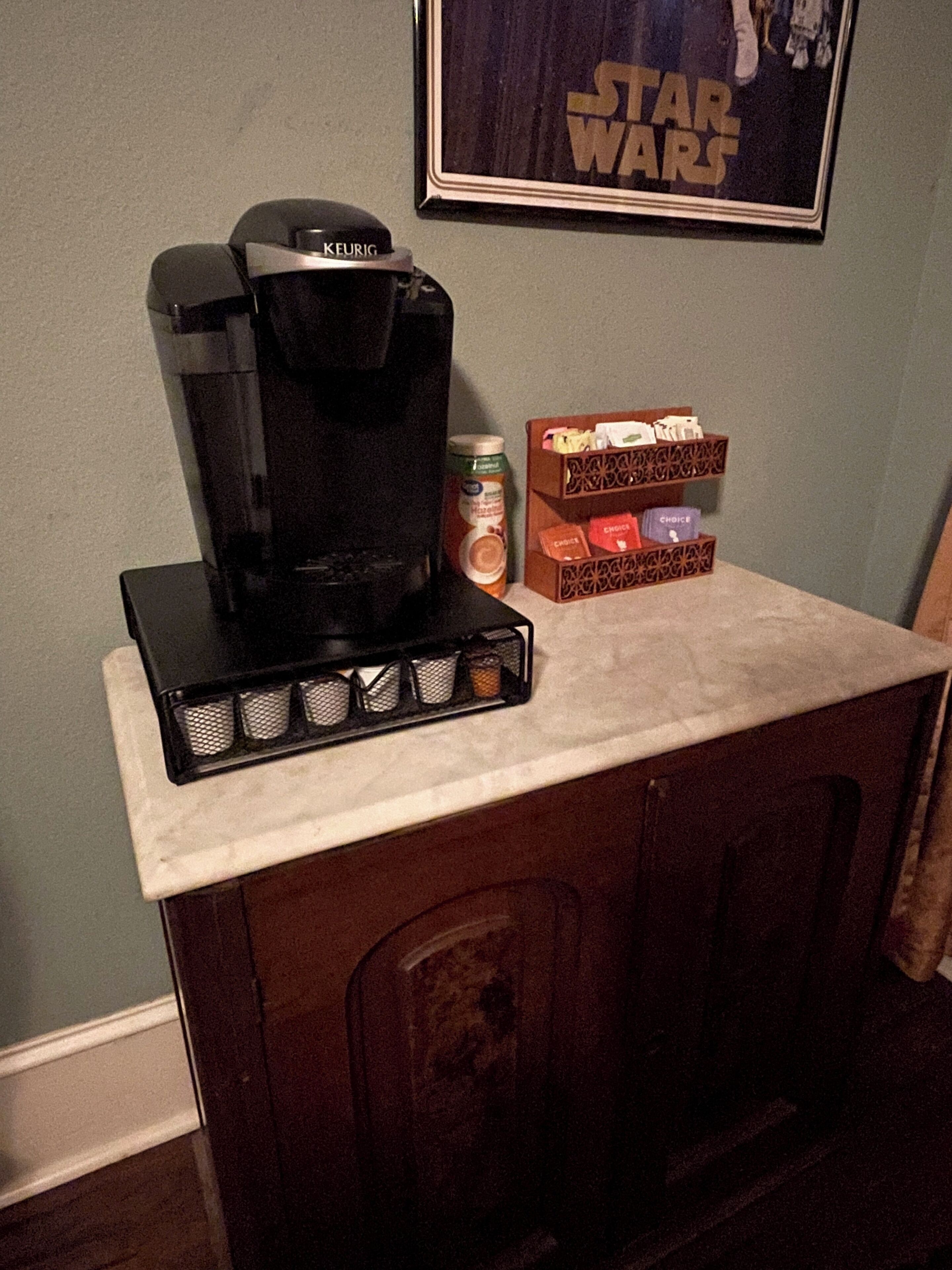 A coffee maker on a countertop with a Star Wars poster on the wall.