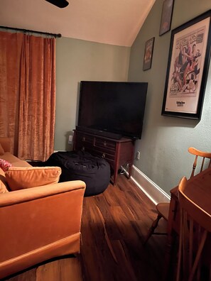 A living room with a flat-screen TV, a wooden cabinet, a bean bag, a wooden dining table, and a framed poster on the wall. -   ⛲️Walk to Lake Eola & restaurants  (Orlando)