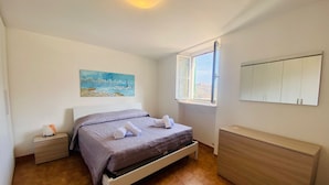 A bedroom with a bed, a nightstand, a dresser, a painting, and a window. - Ca de Matette located just a few minutes' drive from beautiful Finalborgo. (Liguria)