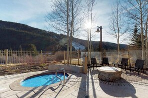 Uma área de piscina com hidromassagem, espaço para sentar ao ar livre e vista para uma montanha arborizada.
