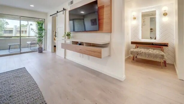 A modern living room with a large TV mounted on the wall, a bench, and a mirror above a vanity. - Walk to Old Town. Heated Pool. Hot tub. Gym. (Scottsdale)