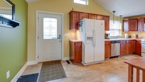 A kitchen with wooden cabinets, a refrigerator, and a window with blinds. - Angola Getaway: Walk to Lake Erie Beach Park! (Angola)