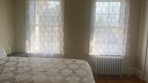 Une chambre à coucher avec un lit, deux fenêtres ornées de rideaux à motifs et un radiateur.