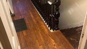 Un escalier en bois avec une balustrade noire, un paillasson en bas et une fenêtre en haut.