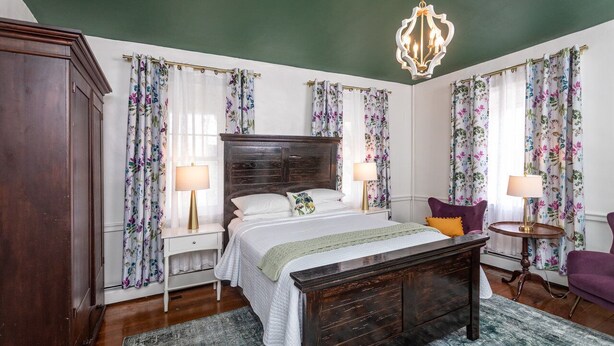 Un dormitorio con una cama grande, dos mesitas de noche, un candelabro y cortinas con motivos florales.