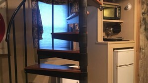 Una escalera de caracol con escalones de madera y barandillas de metal en una cocina con nevera y una ventana con cortinas.