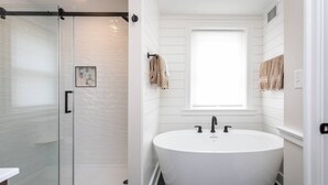 Une salle de bain moderne dotée d’une douche à parois de verre, d’une baignoire sur pieds et d’une fenêtre laissant entrer la lumière naturelle.