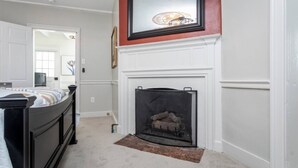 A bedroom with a bed, a fireplace, and a mirror on the wall.
