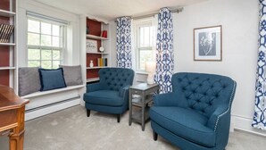 A cozy living room with a built-in bench, two blue armchairs, a small table, and a bookshelf.