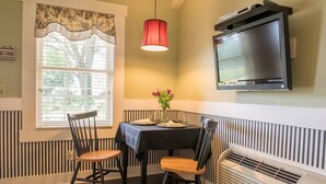 Un coin repas avec une table dressée pour deux personnes, une seule chaise, un vase décoratif et un téléviseur fixé au mur.