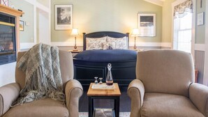 Une chambre à coucher avec un lit, deux lampes de chevet, une petite table avec une bouteille et des verres, et deux fauteuils.