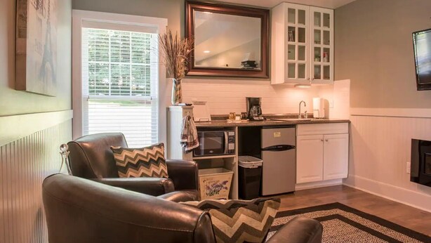 A compact living space with a kitchenette, a dining area with a brown leather chair, and a large window with blinds.