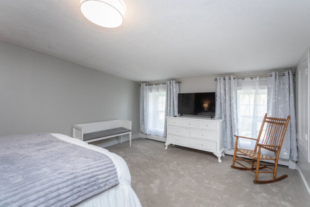 Une chambre à coucher comprenant un lit, une commode, un téléviseur, un fauteuil à bascule et un banc.