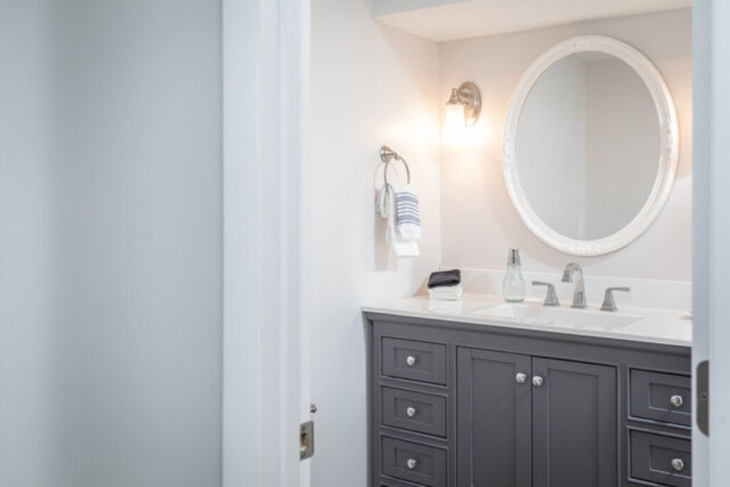 Une salle de bain avec un meuble-lavabo blanc, des armoires sombres, un miroir rond et un porte-serviettes sur lequel est posée une serviette à rayures.